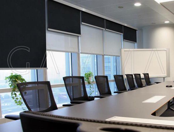 Sala conferenze con sedie scure, tavolo lungo e tende a rullo.