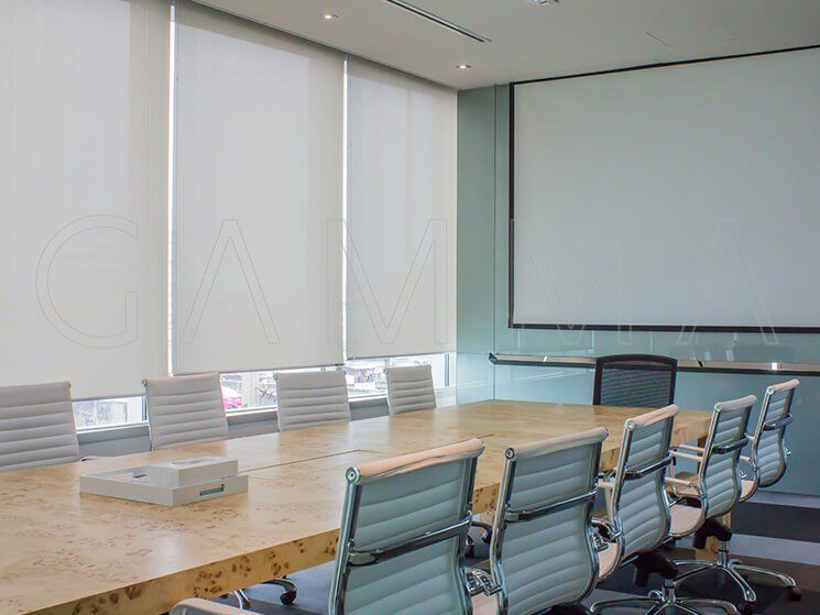 Sala conferenze con un lungo tavolo, sedie, schermo di proiezione e tende alle finestre.
