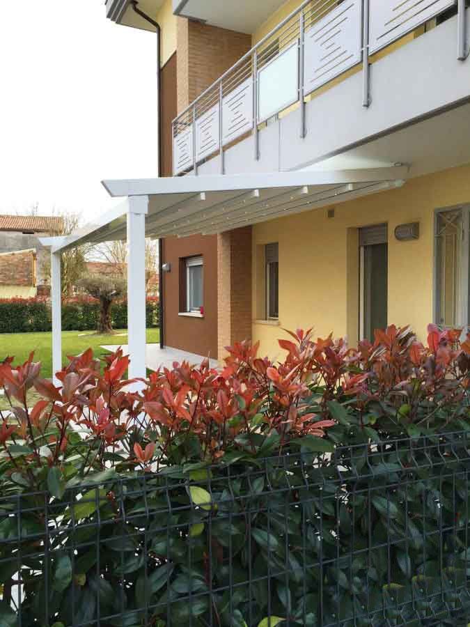 Pergola bianca che si estende da un edificio con una siepe di foglie rosse in primo piano.