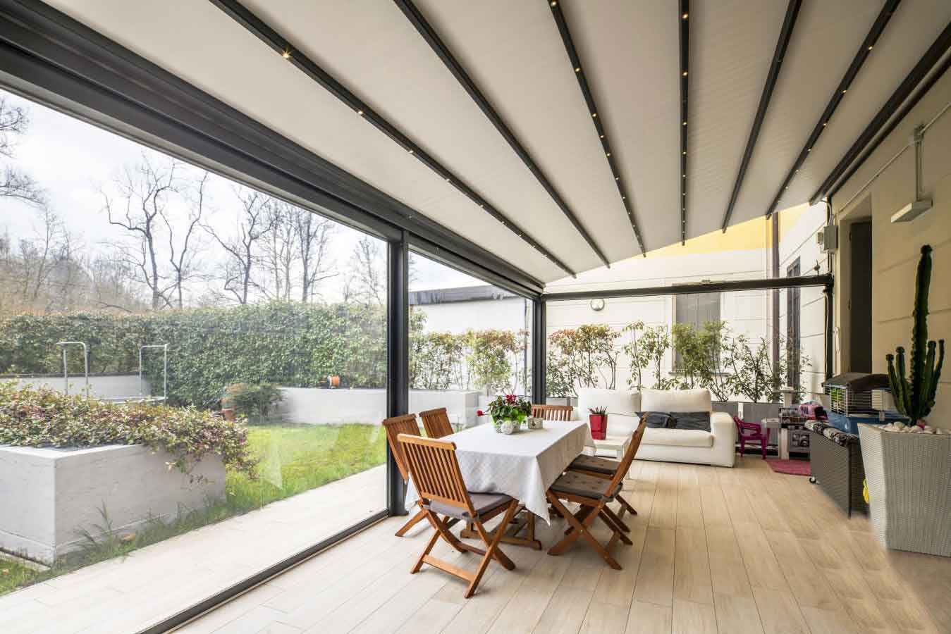 Patio con tetto retrattile, tavolo da pranzo apparecchiato per gli ospiti, con vista su un giardino verde.