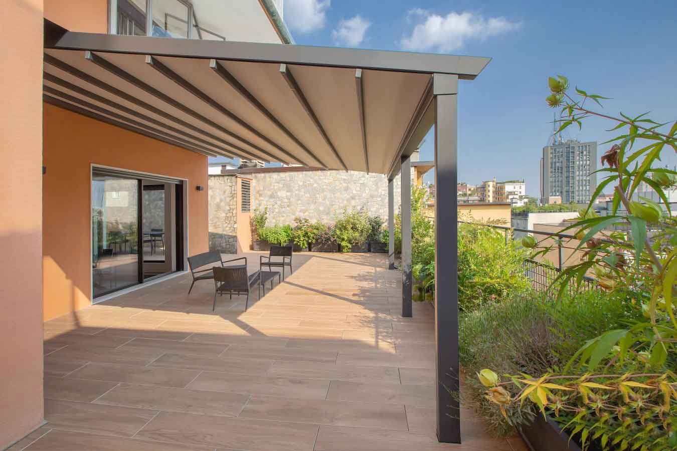 Patio sul tetto con tettoia retrattile, tavolo da pranzo e verde, con la città sullo sfondo.