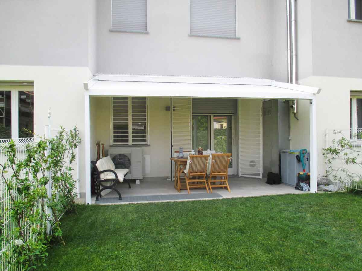 Patio sul retro con tenda da sole bianca, tavolo, sedie e prato verde.
