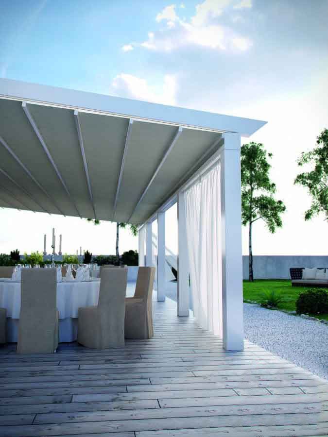 Zona pranzo all'aperto con pergolato bianco, tavoli, sedie e tende trasparenti.