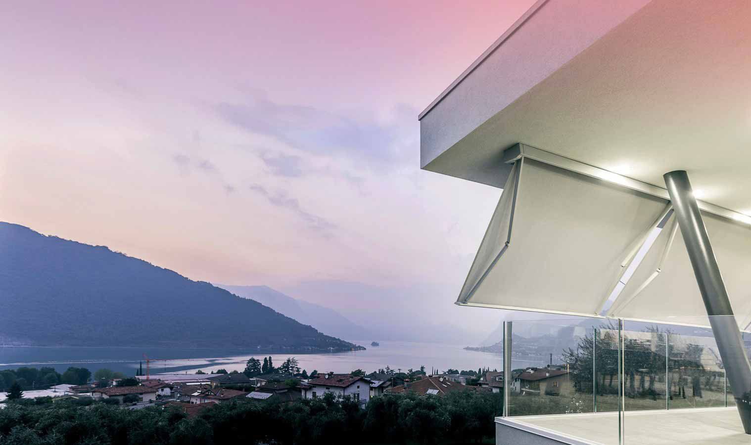 Edificio moderno con tenda da sole bianca che si affaccia su un pittoresco lago e sulla città al tramonto.
