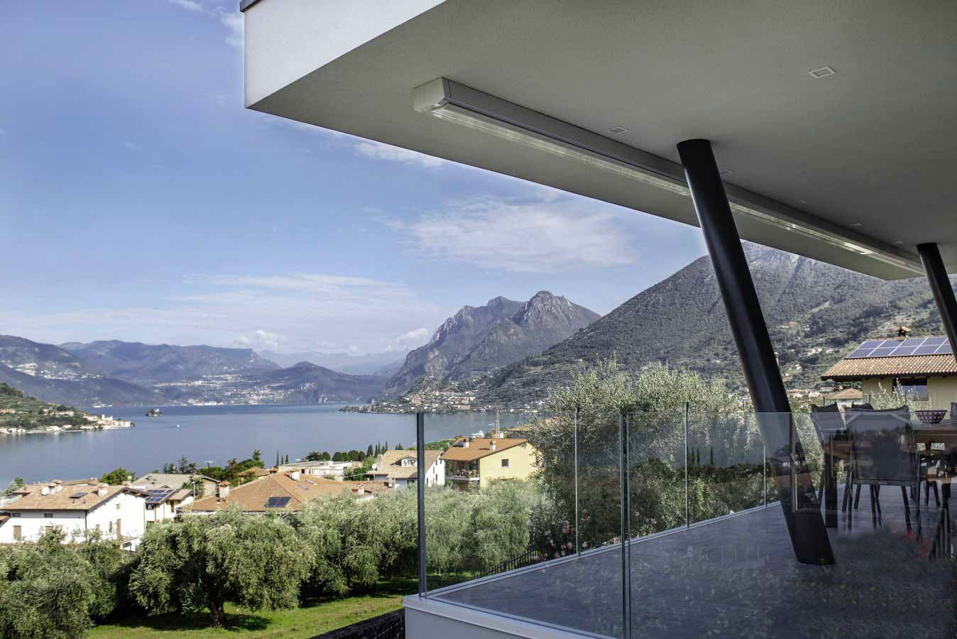 Balcone con vista sul lago, sulle montagne e sulla città sotto un cielo azzurro.