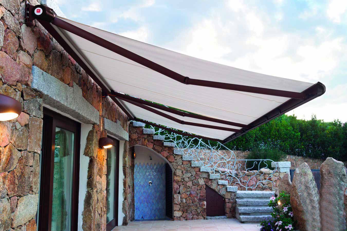Tenda da sole retrattile beige e marrone fissata a un muro di pietra sopra un patio.