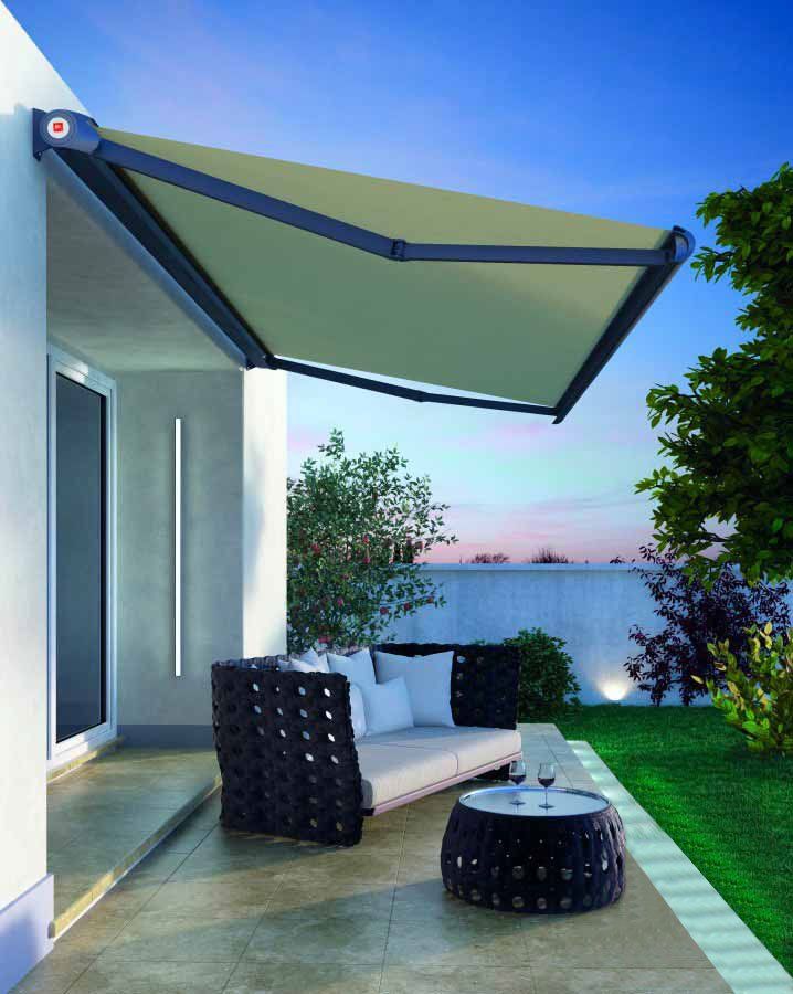 Una tenda da sole retrattile beige protegge un patio con mobili scuri e un giardino.