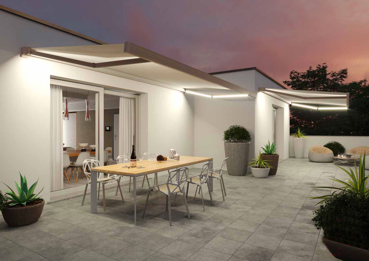 Patio esterno con tavolo da pranzo, sedie, piante e tenda da sole illuminata da luci al tramonto.