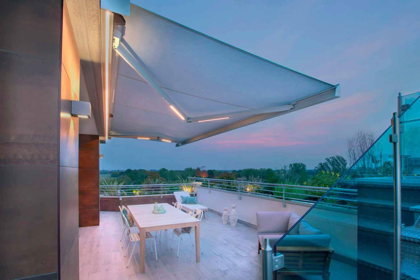 Patio sul tetto con tenda da sole retrattile, tavolo da pranzo e sedie al tramonto.