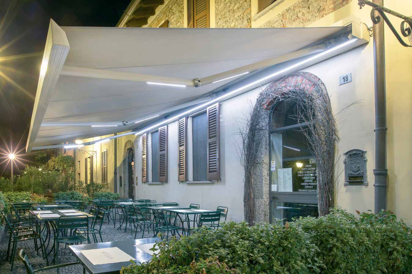 Patio del ristorante di notte con tenda da sole e tavoli/sedie verdi.
