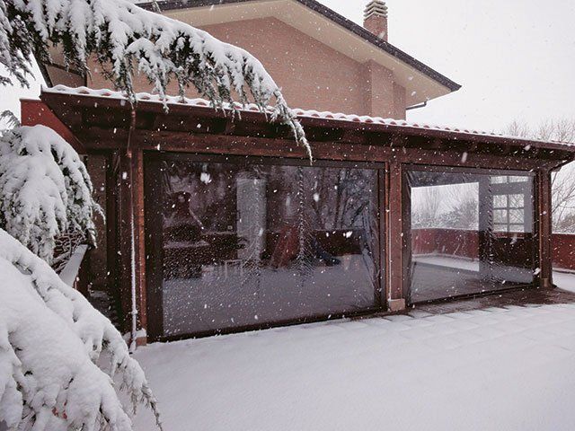 Patio innevato nel cortile sul retro con pareti di plastica trasparente; struttura in legno marrone; neve che cade.