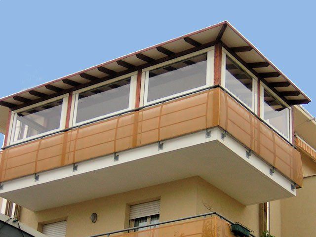 Balcone con pannelli in legno marrone, finestre bianche e tetto ombreggiato; attaccato a un edificio.