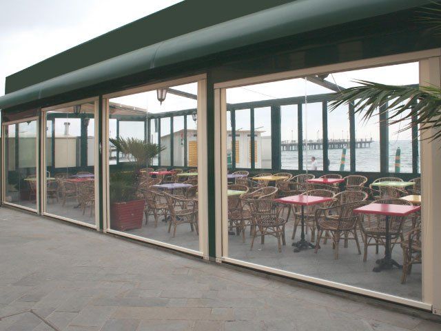 Patio del ristorante con pannelli trasparenti, tavoli, sedie e vista sul molo e sull'oceano.