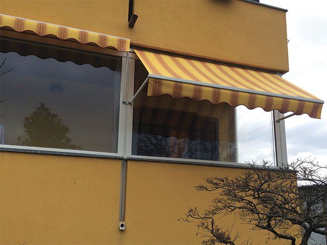 Edificio giallo con tenda a strisce che protegge una finestra.