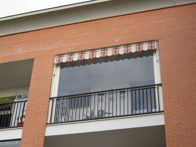 Edificio in mattoni con balcone e tenda a strisce sopra una finestra con zanzariera retrattile.