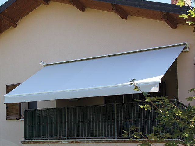 Tenda da sole bianca su un balcone con ringhiera nera, attaccata a un edificio beige.