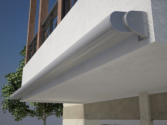 Tenda da sole retrattile grigia fissata a un edificio bianco.
