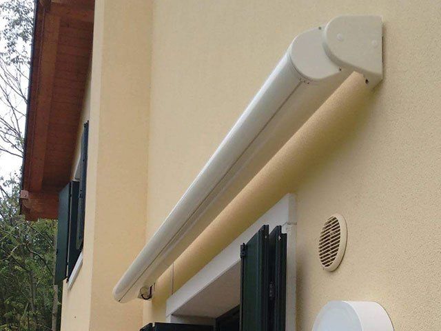 Tenda da sole retrattile bianca montata su un edificio beige sopra una finestra.