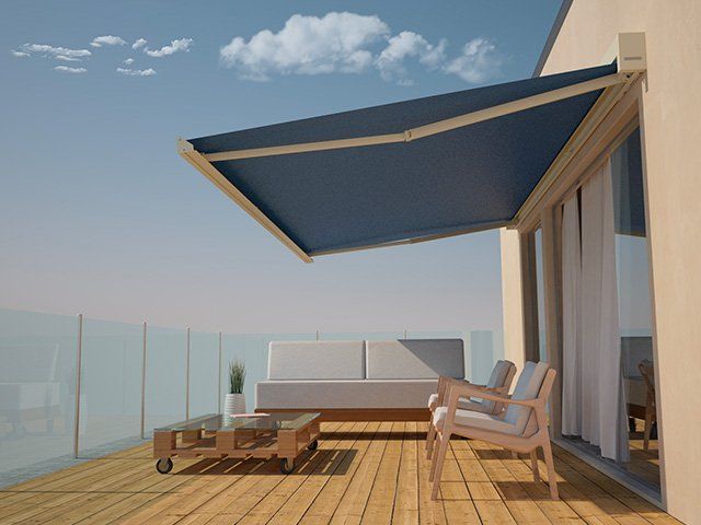 Tenda blu che ombreggia un terrazzo in legno con mobili.