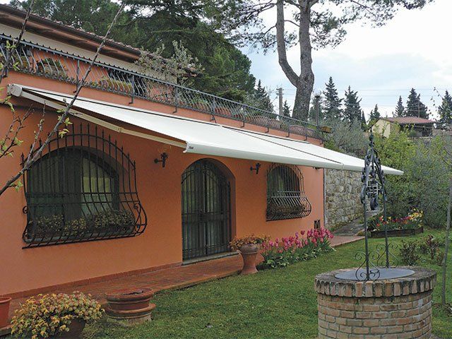 Edificio in stucco arancione con tenda da sole bianca, finestre ad arco e un pozzo nel giardino.
