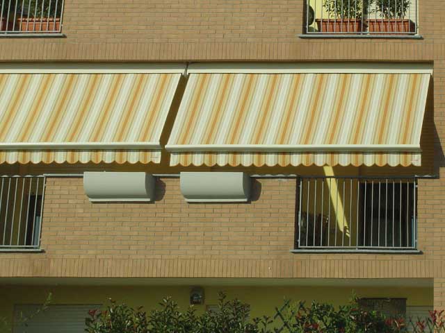 Due tende da sole a strisce gialle e bianche su un edificio in mattoni, sopra le finestre con le sbarre di sicurezza.