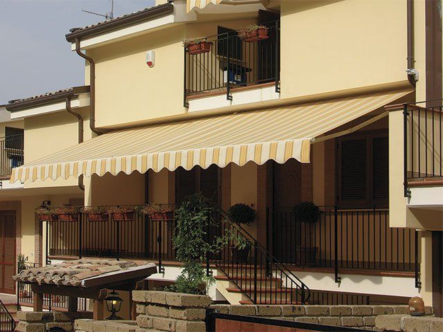 Una tenda a strisce beige protegge il balcone di un edificio color crema a due piani.