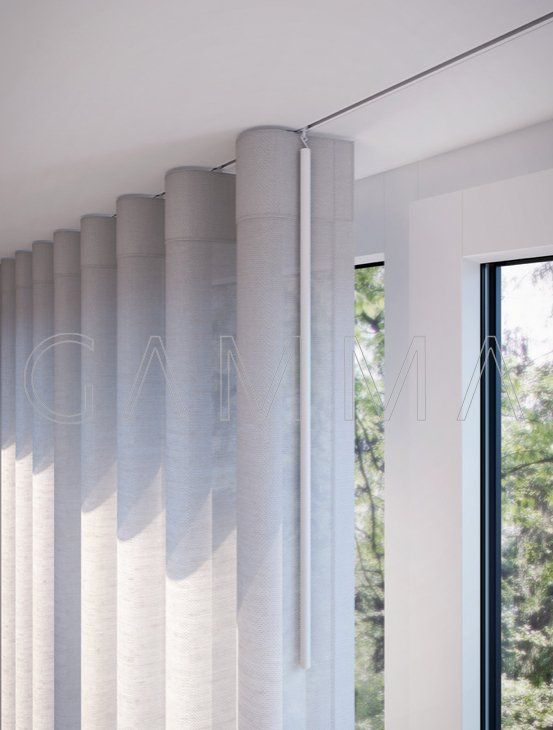 Pannelli verticali grigio chiaro per tende appesi a un binario sul soffitto, accanto a una finestra con alberi visibili.