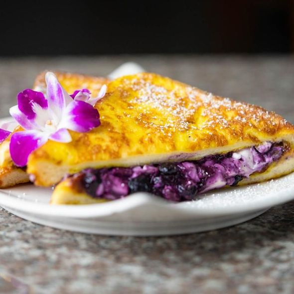 Golden crepe filled with purple berry filling, topped with powdered sugar and an orchid on a white plate