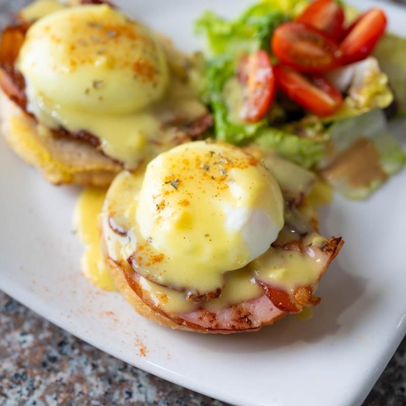 Eggs Benedict with hollandaise, hash browns, and a side salad with cherry tomatoes on a white plate Eggs Benedict with hollandaise, hash browns, and a side salad with cherry tomatoes on a white plate