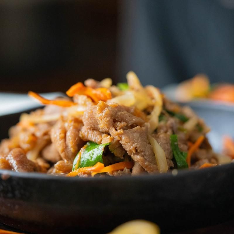 Stir-fried noodles with vegetables and meat in a black bowl, close-up on a dark table. Stir-fried noodles with vegetables and meat in a black bowl, close-up on a dark table.