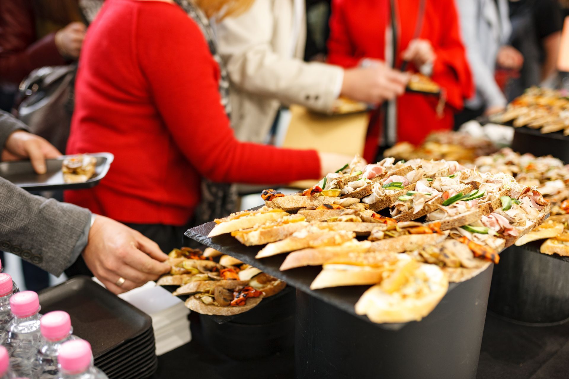 People serving a buffet of toasted sandwiches and toppings at a table outdoors