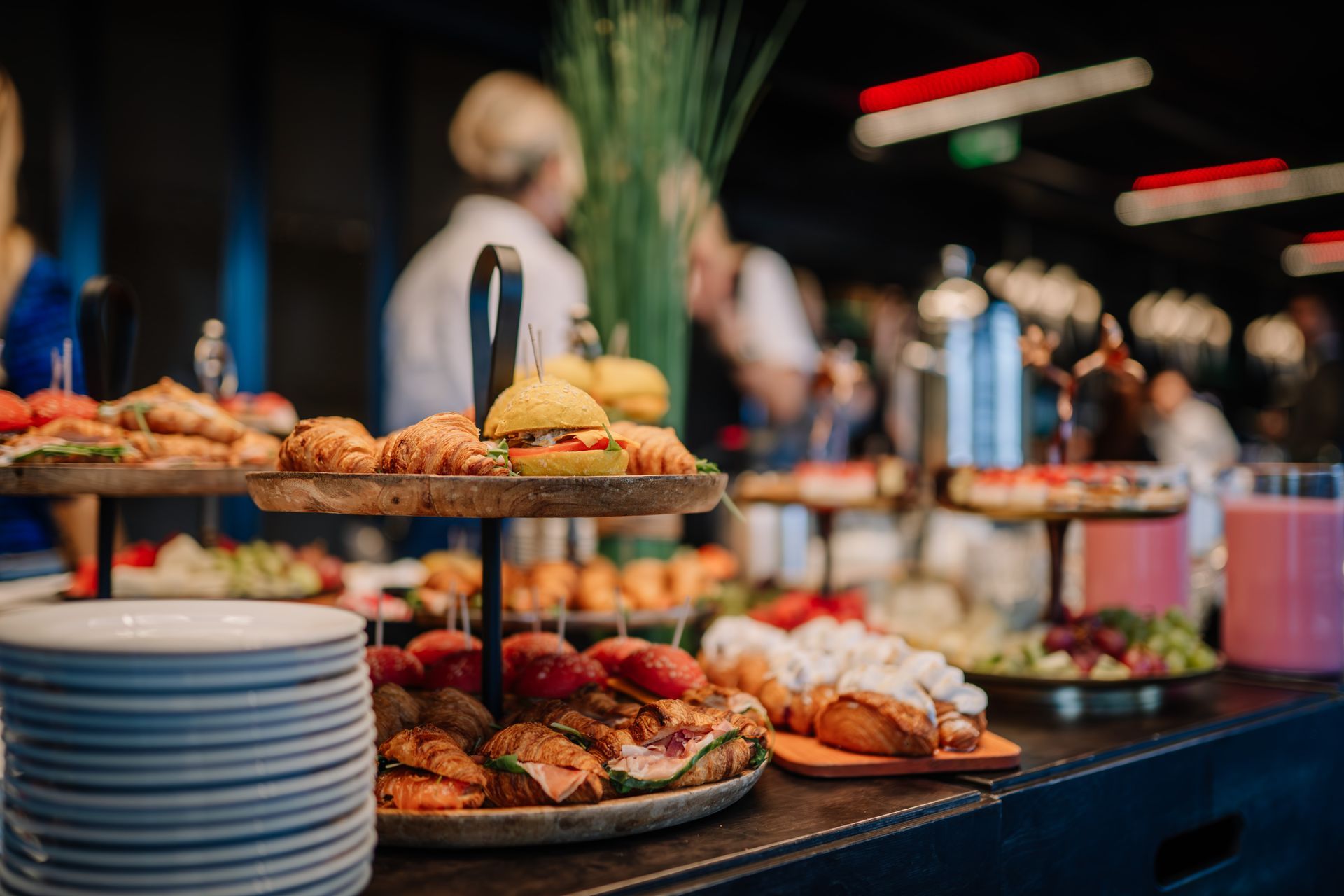 Buffet table with assorted pastries, appetizers, and stacked plates in a blurred restaurant setting