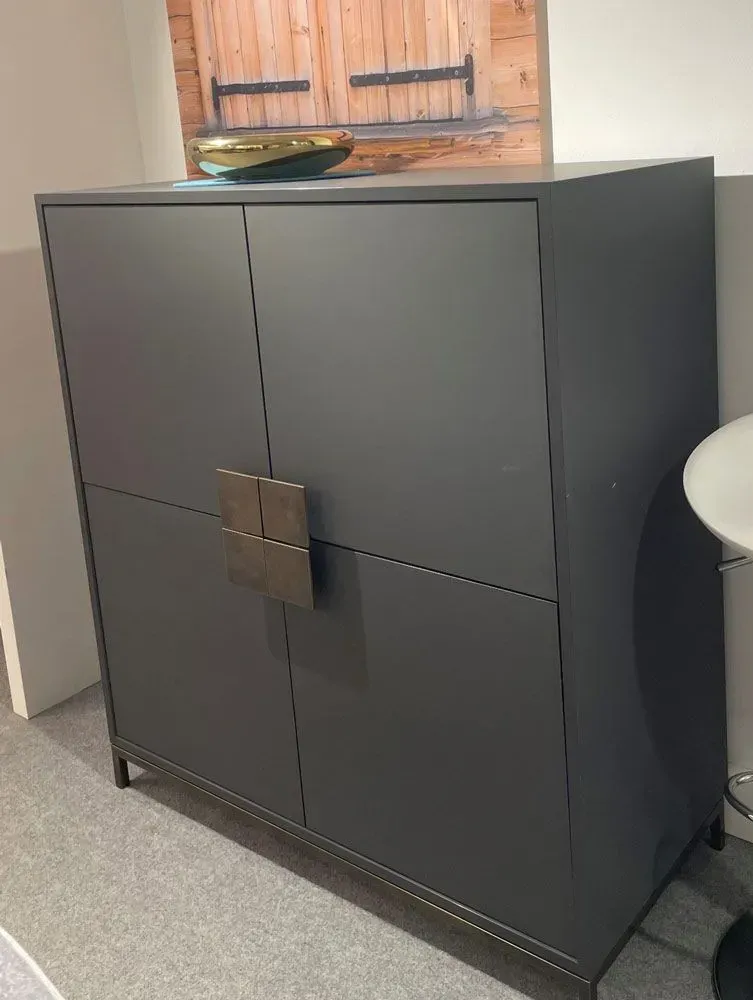 Schwarzer viertüriger Schrank mit quadratischem Griff, der in einem Büro oder Flur steht.