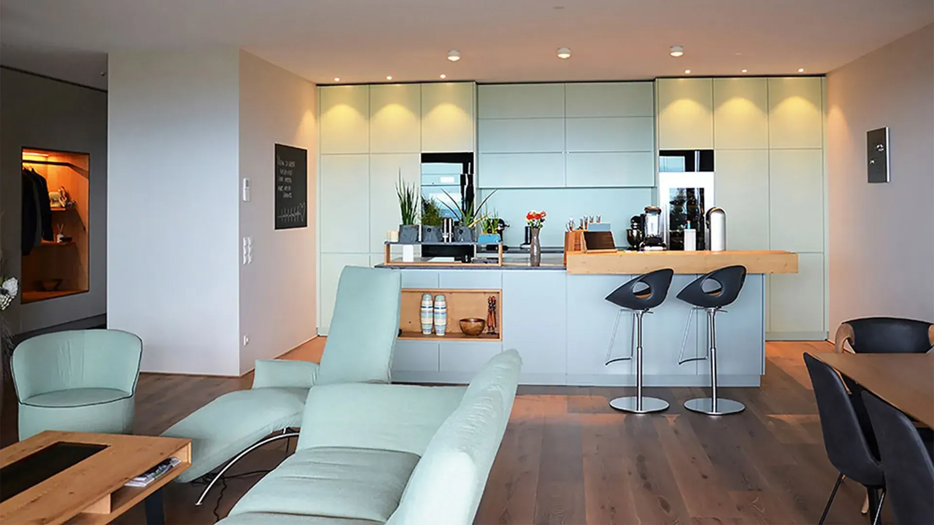 Modernes, offenes Wohnzimmer mit mintgrünem Sofa, Holzboden und Küchenbar mit Barhockern.