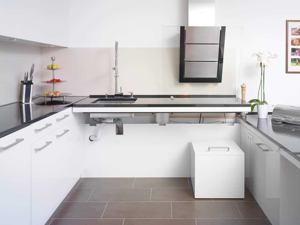 Moderne weiße Küche mit schwarzen Arbeitsplatten, grauem Fliesenboden und Einbaugeräten