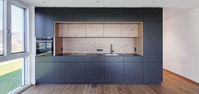 Moderne Küche mit dunkelblauen Schränken, hellem Holzspiegel und großen Fenstern neben einem Holzboden