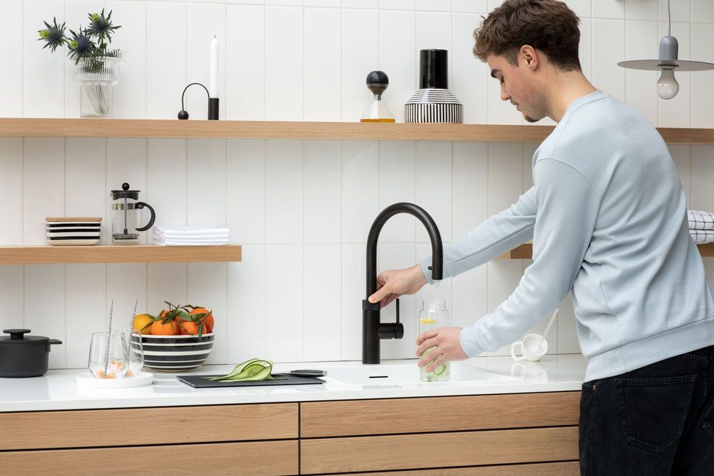 Person wäscht sich in einer hellen, modernen Küche an einem Küchenwaschbecken die Hände.