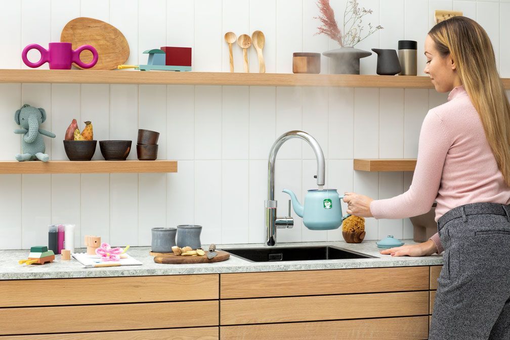 Eine Frau spült Geschirr an einer Küchenspüle mit hellen Holzregalen und mintgrünen Küchengeräten.
