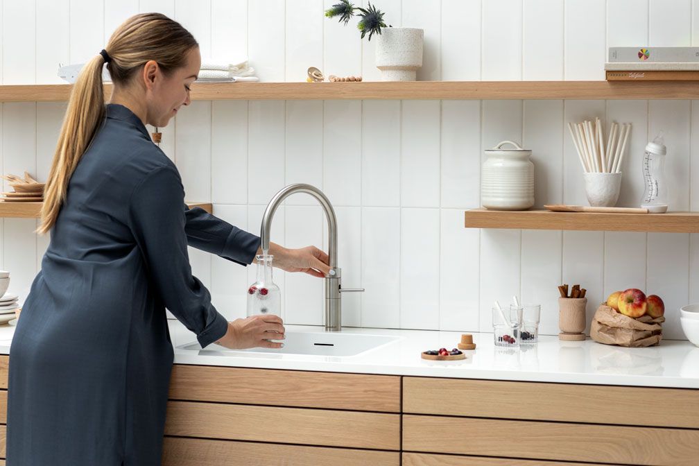 Frau wäscht sich in einer hellen, modernen Küche an einem Küchenwaschbecken die Hände.