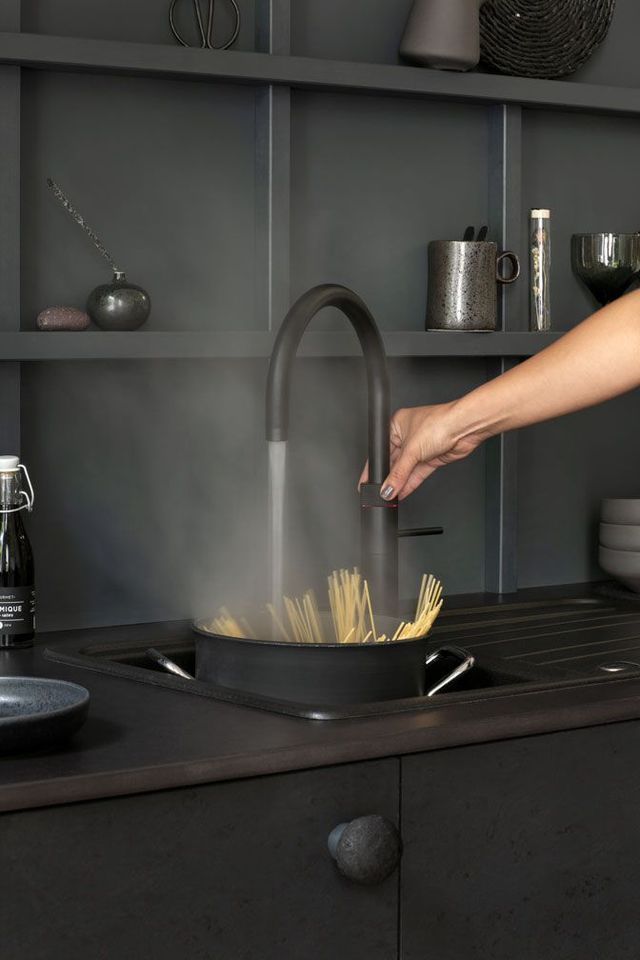 Spaghetti werden von Hand in einem schwarzen Topf unter dem Küchenwasserhahn gerührt, während Dampf aufsteigt.
