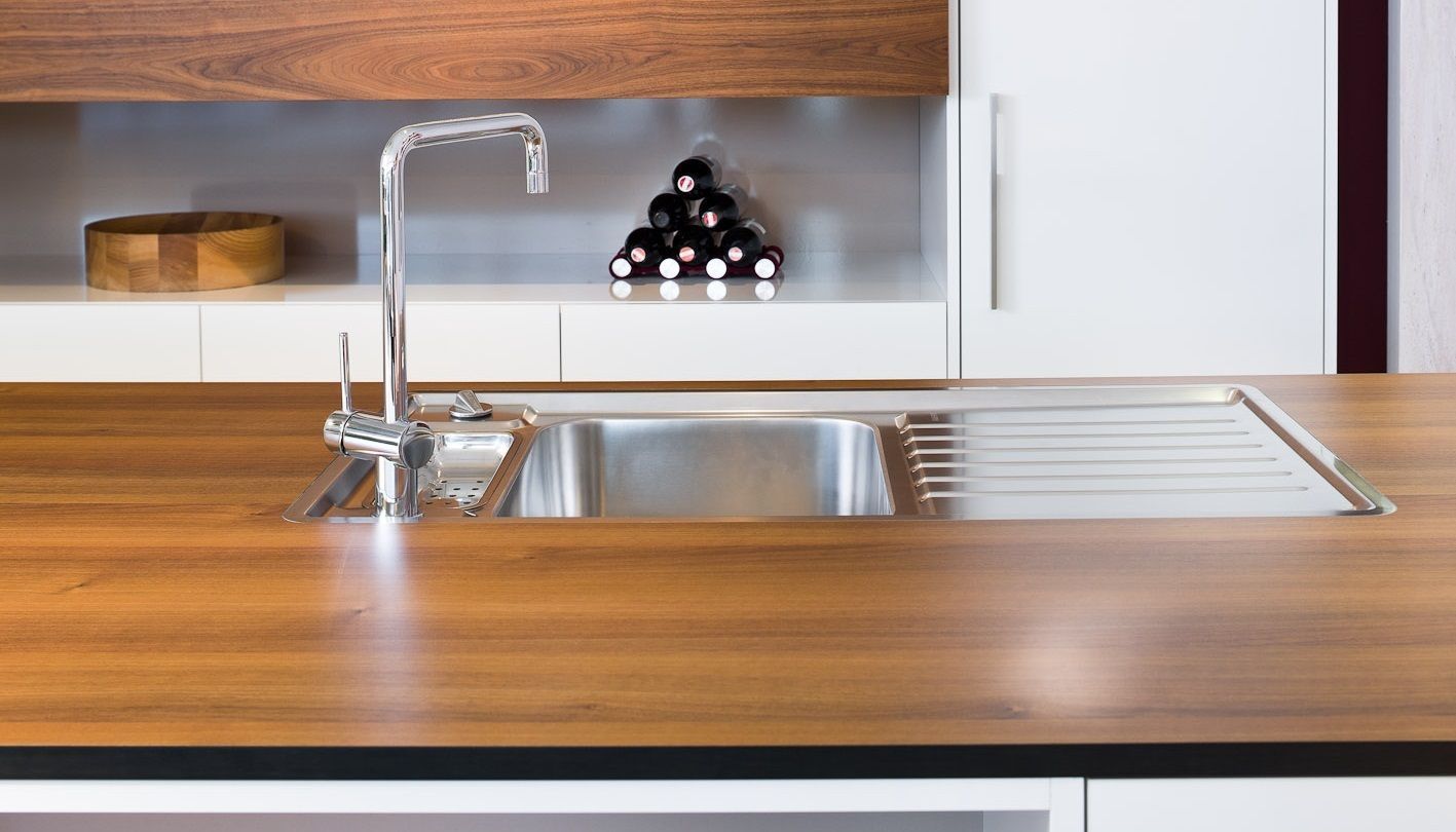 Moderne Küchenarbeitsplatte mit Edelstahlspüle, Chromarmatur und Holzschränken.