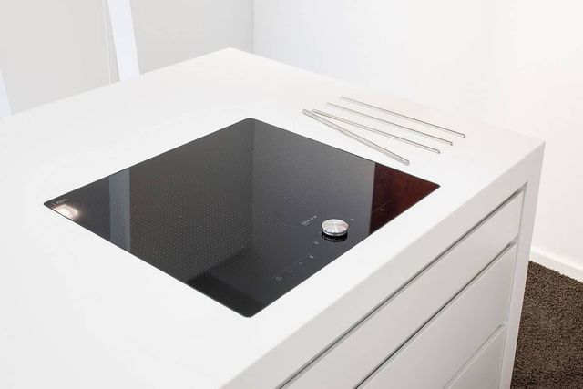 Weiße Küchenarbeitsplatte mit schwarzem Spülbecken und kleinem Wasserhahnknopf, von oben gesehen