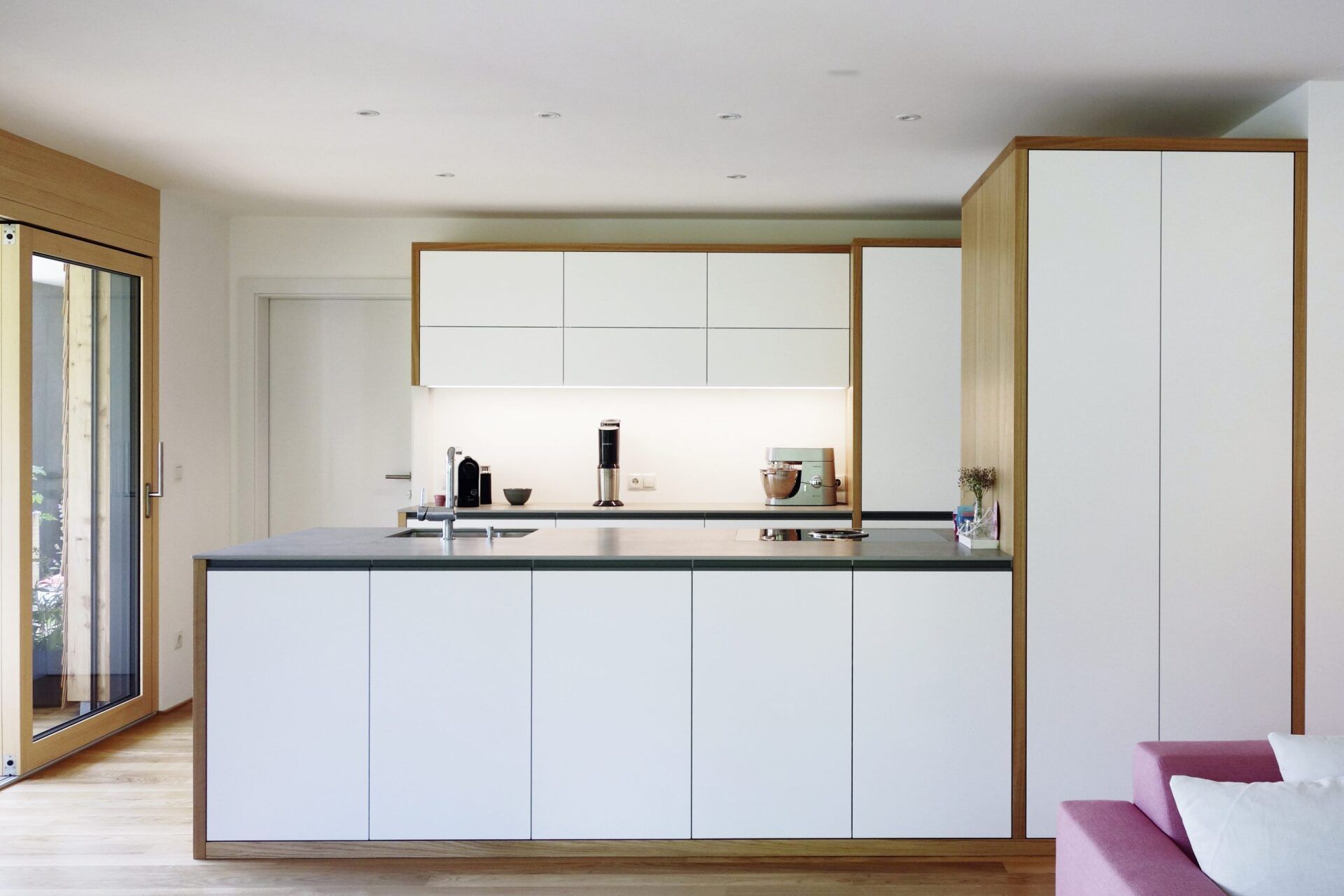Moderne, zeitlose Küche mit weißen Fronten, natürlichen Holzdetails und großzügiger Kücheninsel, geplant und umgesetzt von Hase & Kramer.