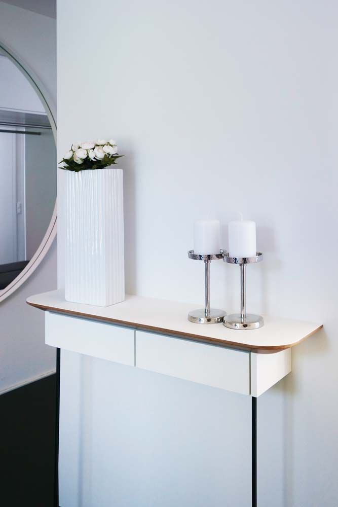 Ein minimalistischer weißer Kaminsims mit Kerzen und einer Vase mit weißen Blumen neben einem runden Spiegel