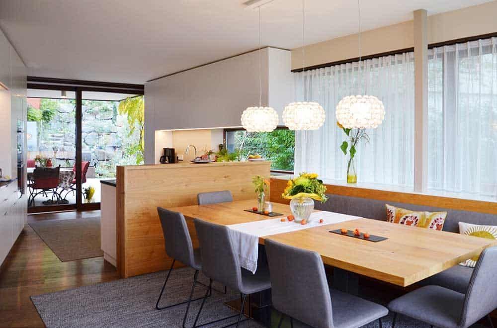 Modernes Esszimmer mit Holztisch, grauen Stühlen, Pendelleuchten und großen Fenstervorhängen.