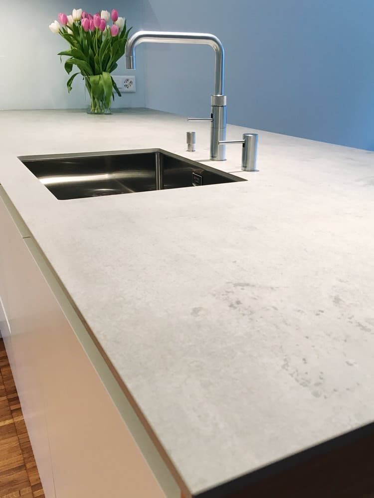 Moderne Kücheninsel mit Edelstahlspüle, Chromarmatur und rosa Blumen auf weißer Arbeitsplatte.