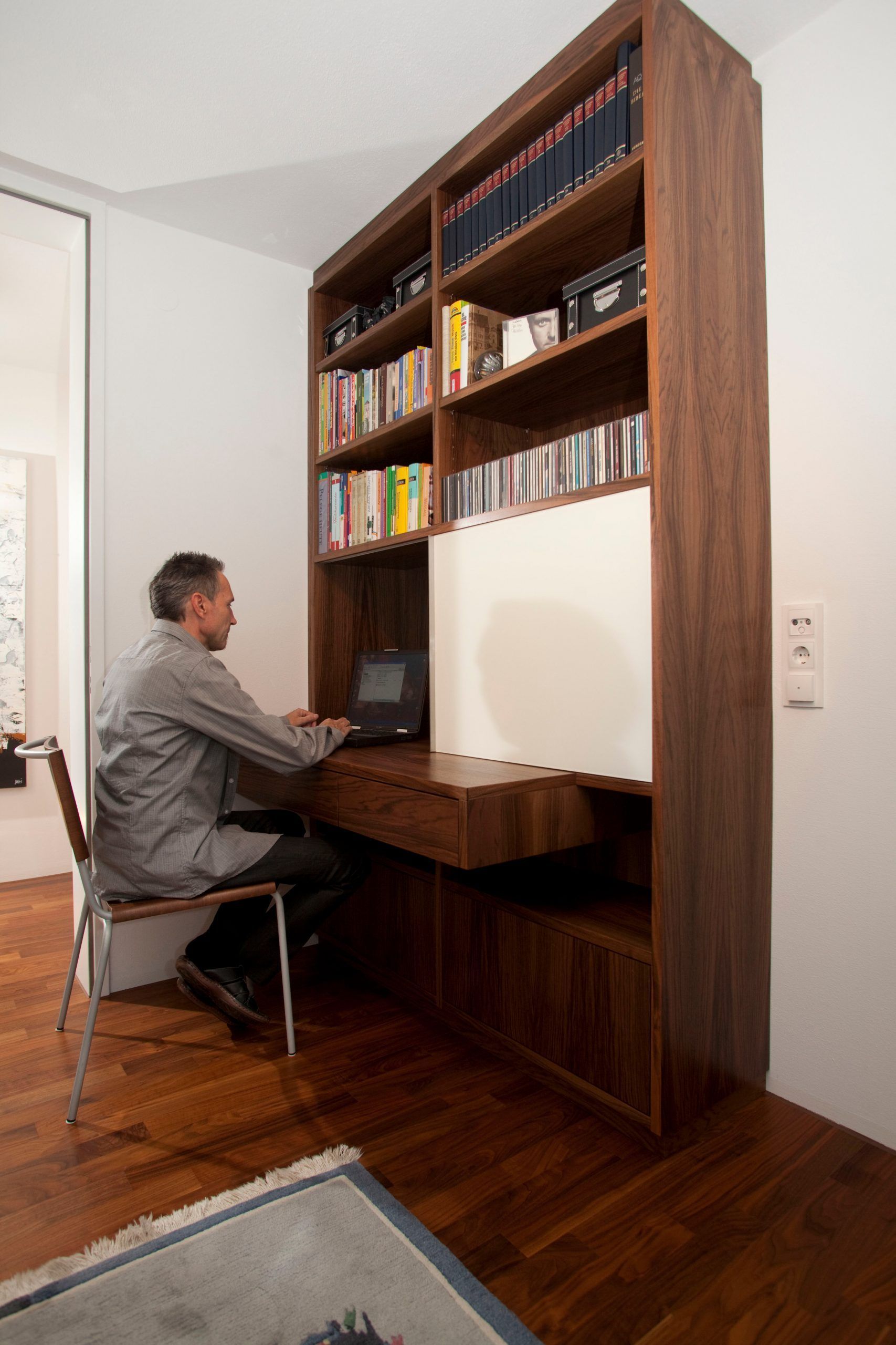 Schreibtisch in einer hohen Nische hinter einem Holzregal und benutzt einen Computer in seinem Heimbüro.