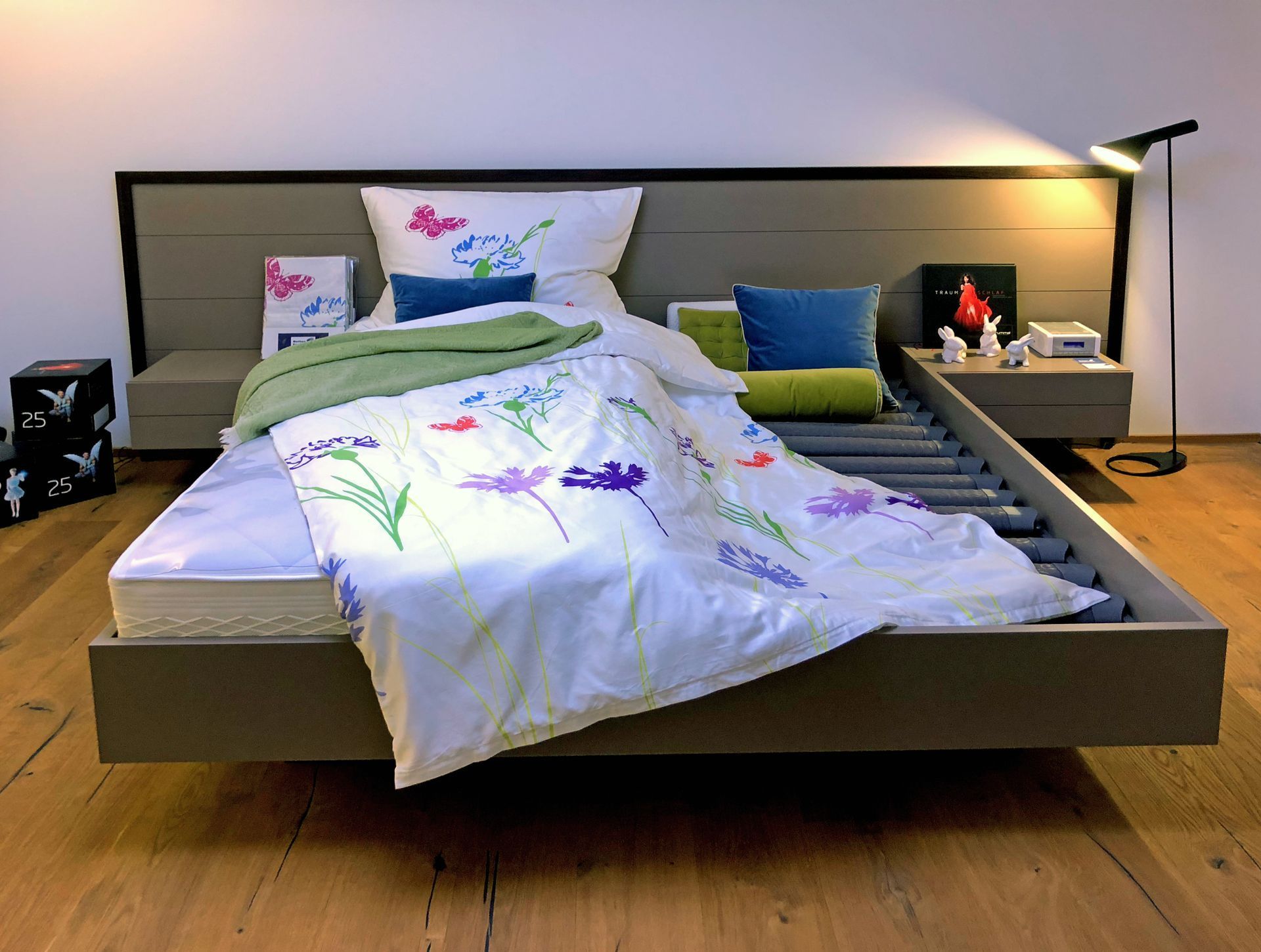 Modernes Schlafzimmer mit niedrigem Bett, weißer Bettwäsche mit Blumenmuster und Nachttischlampen auf Holzboden