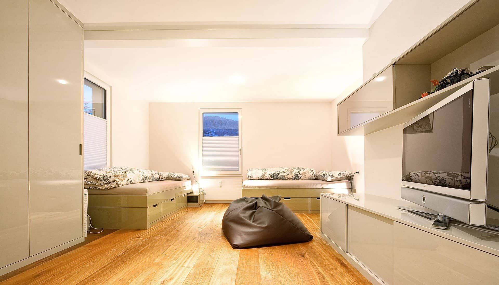 Helles, modernes Schlafzimmer mit Holzboden, Bett, Fernsehschrank und Fenster mit Jalousien.