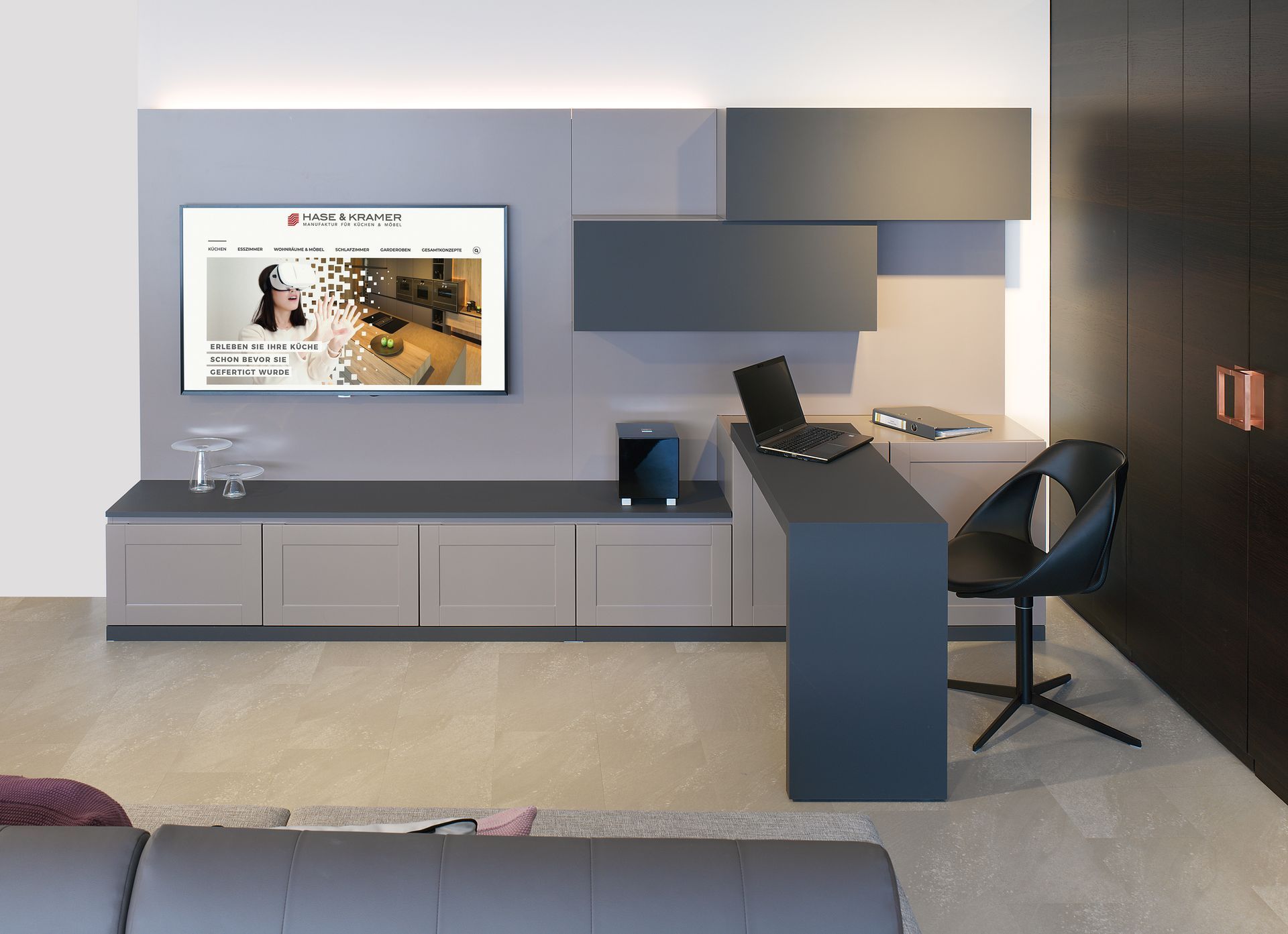 Modernes Hotelzimmer mit an der Wand montiertem Fernseher, niedrigem Schrank, Schreibtisch und Stuhl in Grau- und Blautönen.